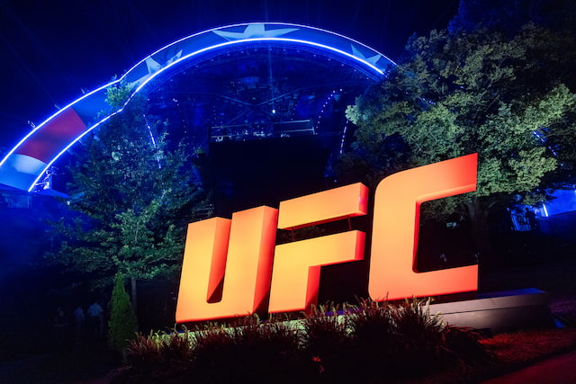 Illuminated orange UFC sign beneath blue event lighting at night.