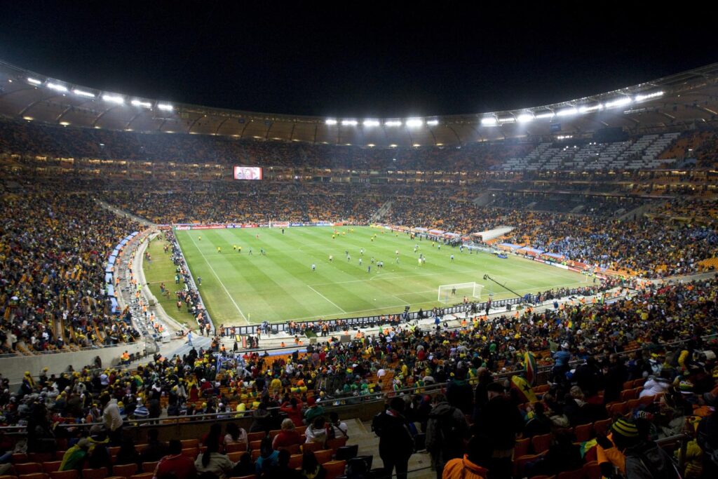 Wide view of FNB Stadium under floodlights, with spectators surrounding the pitch.