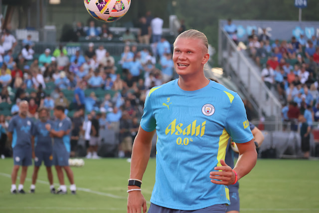 Erling Haaland watches a football during a Manchester City open training session, with supporters in the background.
