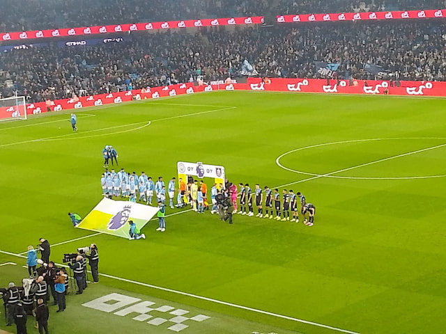 Manchester City and Burnley line up beside a Premier League banner at the Etihad Stadium, with supporters filling the stands behind them.