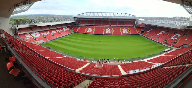 Panoramic view of Anfield with its green pitch and red Liverpool stands.